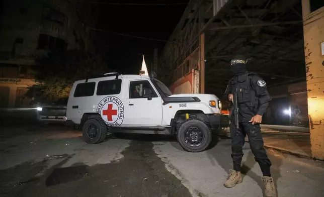 A gunman wearing the uniform of the al-Qassam Brigades, the military wing of Hamas, stands guard as Red Cross vehicles enter a warehouse allegedly to collect coffins containing the bodies of four deceased hostages, in Gaza City, Tuesday, Oct. 14, 2025. (AP Photo/Yousef Al Zanoun)