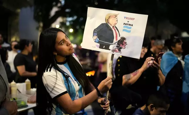A woman holds a banner reading in Spanish, "Trump or homeland," outside former President Cristina Fernandez's home, where she is serving a six-year house arrest sentence for corruption, after polls closed during legislative midterm elections in Buenos Aires, Argentina, Sunday, Oct. 26, 2025. (AP Photo/Natacha Pisarenko)
