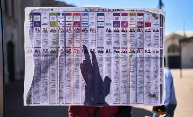 A woman points on the list of candidates placed outside a polling station during legislative midterm elections in Buenos Aires, Argentina, Sunday, Oct. 26, 2025. (AP Photo/Rodrigo Abd)