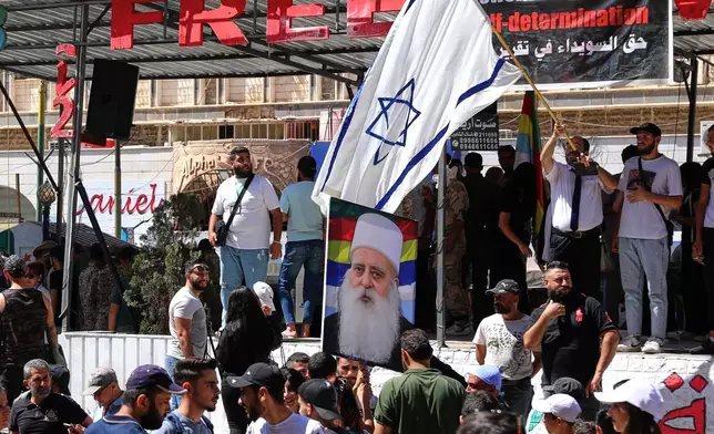 A man waves an Israeli flag over a picture of Sheikh Mowafak Tarif, the spiritual leader of the Druze in Israel, during a weekly rally in Sweida, southern Syria, on Sept. 20, 2025. (AP Photo/Fahd Kiwan)