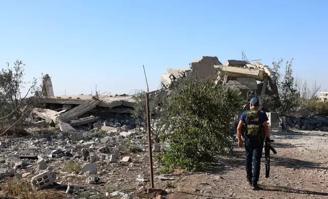 A gunman walks by the remains of a house destroyed during the recent sectarian clashes in the Druze-majority town of Sweida, southern Syria, on Sept. 19, 2025. (AP Photo/Fahd Kiwan)