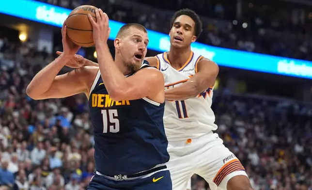 Denver Nuggets center Nikola Jokic, left, pulls in a rebound as Phoenix Suns forward Oso Ighodaro, right, defends in the first half of an NBA basketball game Saturday, Oct. 25, 2025, in Denver. (AP Photo/David Zalubowski)