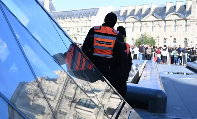 Private security members watch people queueing outside the Louvre museum, Thursday, Oct. 30, 2025 in Paris. (AP Photo/Emma Da Silva)