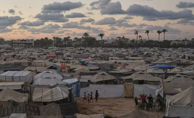 Dusk falls as a group of Palestinians sit outside a tent at a temporary camp in Deir al-Balah, in the central Gaza Strip, Monday, Oct. 6, 2025. (AP Photo/Abdel Kareem Hana)
