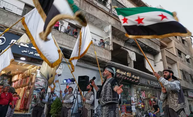 Residents watch a celebration below marking the opening of a new shop in the Damascus suburb of Daraya, Syria, Saturday, Oct. 4, 2025, ahead of a parliamentary election set to take place Sunday. (AP Photo/Omar Sanadiki)