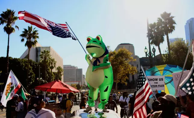 A protester wearing an inflatable frog costume and waving an American flag takes part in a "No Kings" protest Saturday, Oct. 18, 2025, in Los Angeles. (AP Photo/Ethan Swope)