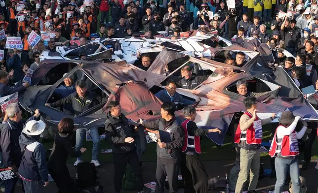 Protesters tear a banner with a face image of U.S. President Donald Trump during a rally in Gyeongju, South Korea, Wednesday, Oct. 29, 2025. (AP Photo/Lee Jin-man)