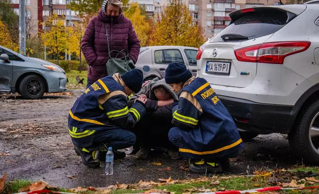 Emergency workers comfort a man who lost his son in Russia's drone attack that hit residential buildings in Kyiv, Ukraine, Sunday, Oct. 26, 2025. (AP Photo/Dan Bashakov)