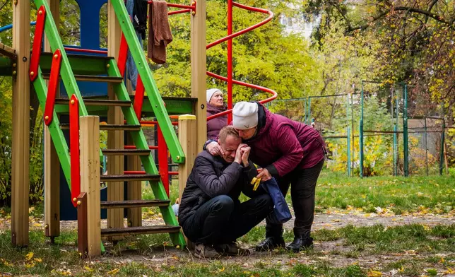 Neighbors comfort a man who lost his son in Russia's drone attacks that hit residential buildings in Kyiv, Ukraine, Sunday, Oct. 26, 2025 (AP Photo/Dan Bashakov)