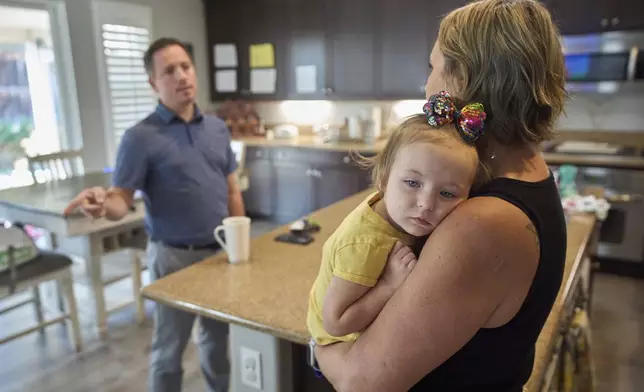 Emily Marris, right, holds her daughter, Brooklyn Marris, as she talks to her husband, Josh Marris, at their home in Winchester, Calif., on Thursday, Sept. 18, 2025. (AP Photo/Gregory Bull)