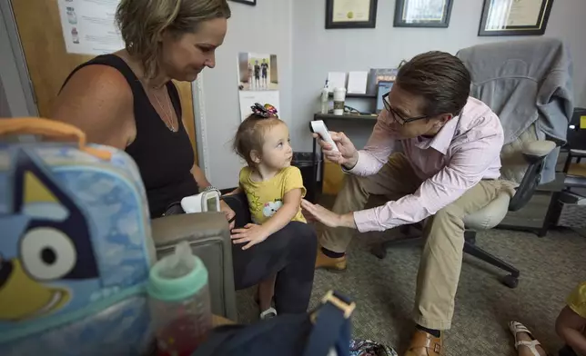 Dr. Charles Fraley, right, checks the temperature of Brooklyn Marris, center, as she arrives for a blood pressure check with her mother, Emily Marris, left, at his office in Winchester, Calif., on Thursday, Sept. 18, 2025. (AP Photo/Gregory Bull)