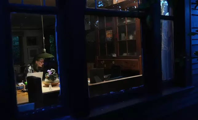 Seeing through the window, Mary E. Brunkow is seen answering messages and emails after winning a Nobel Prize in medicine for part of her work on peripheral immune tolerance, in Seattle, Monday, Oct. 6, 2025. Next to her is her dog Zelda. (AP Photo/Lindsey Wasson)