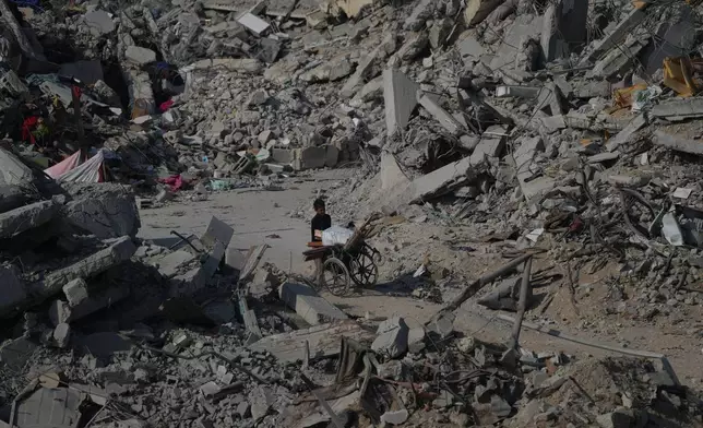 A boy pushes a wheelchair through the rubble of buildings destroyed in the war between Israel and Hamas, in the al-Nafaq area of the Sheikh Radwan neighborhood in Gaza City, Friday, Oct. 24, 2025. (AP Photo/Abdel Kareem Hana)