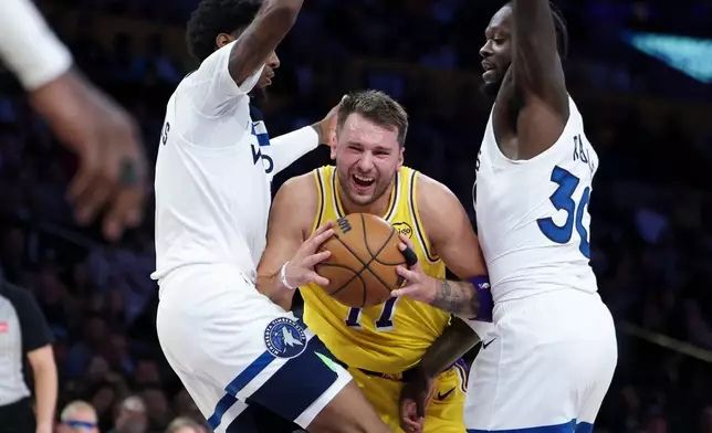 Los Angeles Lakers guard Luka Doncic, center, drives against Minnesota Timberwolves forward Jaden McDaniels, left, and forward Julius Randle during the first half of an NBA basketball game, Friday, Oct. 24, 2025, in Los Angeles. (AP Photo/Jessie Alcheh)