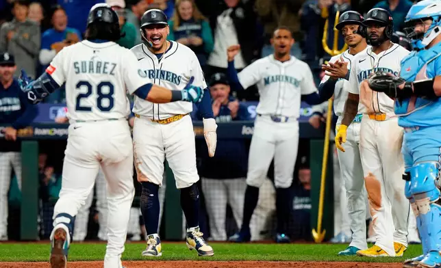 Seattle Mariners' Eugenio Suárez (28) comes in to celebrate with teammates after hitting a grand slam during the eighth inning of Game 5 of baseball's American League Championship Series against the Toronto Blue Jays in Seattle, Friday, Oct. 17, 2025. (Frank Gunn/The Canadian Press via AP)
