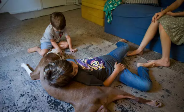 Taylor Moyer and two of her sons play with their pet dog, Roscoe, in the living room at home, Sunday, Oct. 5, 2025, in Virginia Beach, Va. (AP Photo/John Clark)