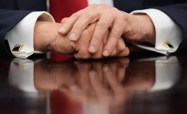 President Donald Trump rests his hands on the Resolute Desk as he speaks to reporters before signing an executive order in the Oval Office at the White House, Monday, Oct. 6, 2025, in Washington. (AP Photo/Jacquelyn Martin)
