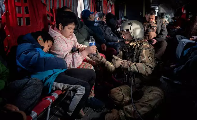 In this photo provided by the Alaska Army National, Guard Sgt. Mary Miller, a helicopter crew chief, passes a bottle of water to a child while evacuating displaced people from Kwigillingok, Alaska, during recovery operations on Thursday, Oct. 16, 2025. (Joseph Moon/Alaska National Guard via AP)