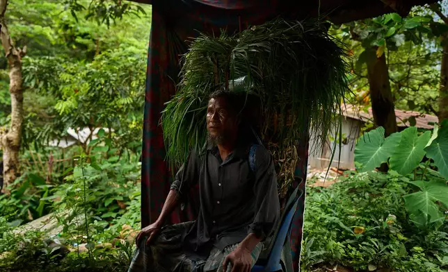 Mahmud Karmar poses for a portrait with a basket of grass he spent the morning gathering to feed his family's cow in the Tak province of Thailand, Thursday, Aug. 28, 2025. (AP Photo/Bram Janssen)