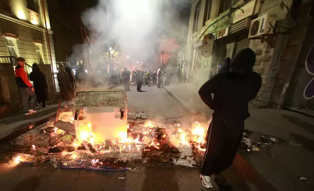 A demonstrator stands behind a burning barricade not far from a police line during an opposition rally in the city center of Tbilisi, Georgia, on Sunday, Oct. 5, 2025, boycotting the municipal elections and calling for the release of political opponents. (AP Photo/Zurab Tsertsvadze)