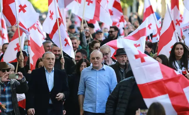 Paata Burchuladze, opera singer and one of the organizers of the rally, center left, and former Chief Prosecutor of Georgia Murtaz Zodelavaother, center, march with other opposition supporters carrying Georgian national flags in the city center of Tbilisi, Georgia, on Saturday, Oct. 4, 2025, boycotting the municipal elections and calling for the release of political opponents. (AP Photo/Zurab Tsertsvadze)