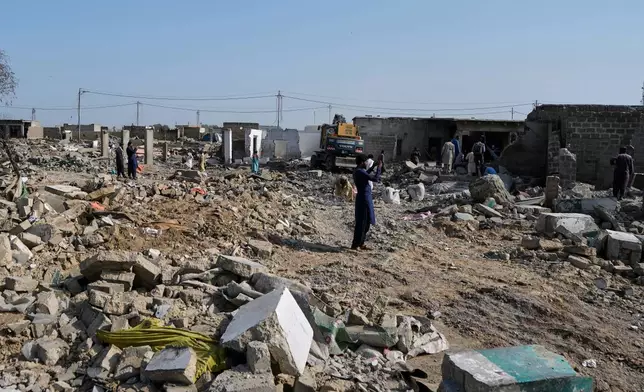 People walk through rubble as a hydraulic shovel demolish a structure during an operation against illegal settlement of Afghan refugees conducted by local government, on the outskirts of Karachi, Pakistan, Wednesday, Oct. 15, 2025. (AP Photo/Fareed Khan)