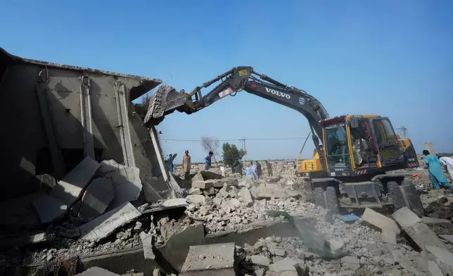 A hydraulic shovel demolish a structure during an operation against illegal settlement of Afghan refugees conducted by local government, on the outskirts of Karachi, Pakistan, Wednesday, Oct. 15, 2025. (AP Photo/Fareed Khan)