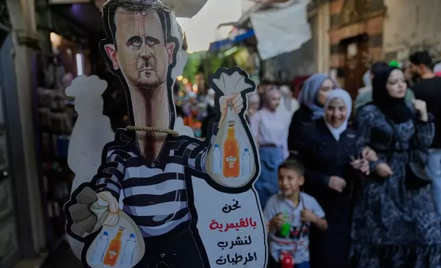 A cutout caricature shows the former Syrian president Bashar Assad sells soft drinks in the old city of Damascus, Syria, Thursday, Oct. 2, 2025. (AP Photo/Hussein Malla)
