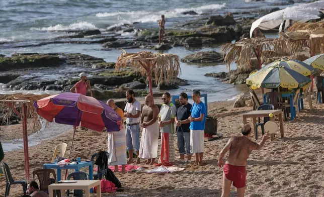 Syrian men attend their noon prayer, left, as others play racket ball at a public beach on the Mediterranean sea, in the coastal city of Latakia, Syria, Sunday, Oct. 5, 2025. (AP Photo/Hussein Malla)
