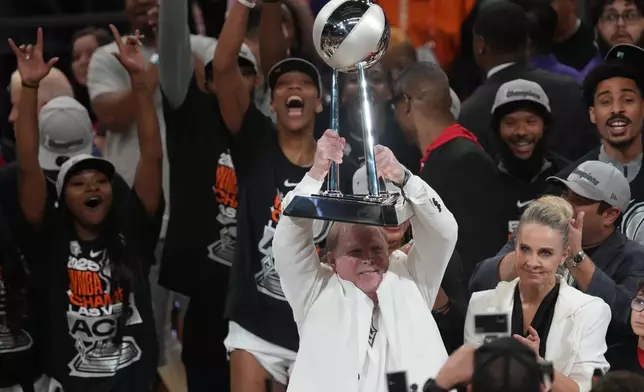 Las Vegas Aces owner Mark Davis, center, holds up the championship trophy after defeating the Phoenix Mercury in Game 4 of the WNBA basketball finals, Friday, Oct. 10, 2025, in Phoenix. (AP Photo/Rick Scuteri)