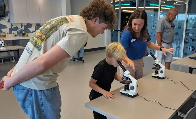 Staff member Amanda Shuman, second from right, instructs visitors using microscopes in the biomedical and immunology teaching laboratory at the Mote Science Education Aquarium, Monday, Oct. 6, 2025, in Sarasota, Fla. (AP Photo/Chris O'Meara)