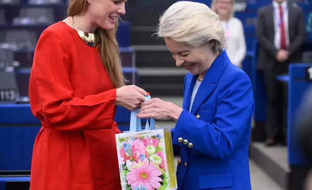 European Commission president Ursula von der Leyen, right, gets a gift for her birthday before delivering her statement on EU response to recent Russian violations of the EU Member States' airspace and critical infrastructure, Wednesday, Oct. 8, 2025 at the European Parliament in Strasbourg, eastern France. (AP Photo/Pascal Bastien)