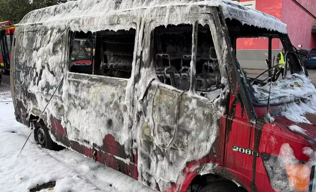 A burned van is covered by extinguishing foam after a fire in Munich, Germany, Wednesday, Oct. 1, 2025. (Roland Freund/dpa via AP)