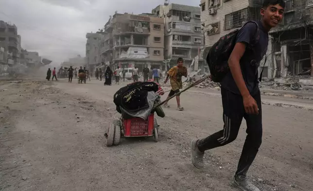 Displaced Palestinians walk with their belongings along the heavily damaged Al-Jalaa Street in Gaza City, Sunday, Oct. 12, 2025, after Israel and Hamas agreed to a pause in their war and the release of the remaining hostages. (AP Photo/Abdel Kareem Hana)