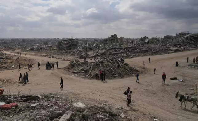 Displaced Palestinians walk amid destroyed buildings in Al-Jalaa Street in Gaza City, Sunday, Oct. 12, 2025, after Israel and Hamas agreed to a pause in their war and the release of the remaining hostages. (AP Photo/Abdel Kareem Hana)