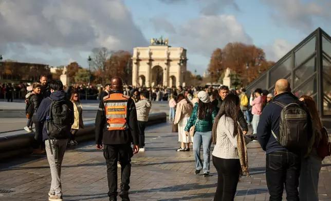 A member of a private security company, center, and visitors walk in the courtyard of the Louvre museum, Sunday, Oct. 26, 2025 in Paris. The Paris prosecutor said that a number of suspects have been arrested over the theft of crown jewels from Paris' Louvre museum last weekend. (AP Photo/Thomas Padilla)