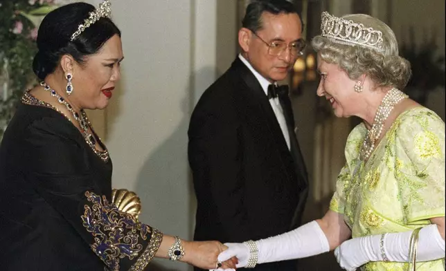 FILE - British Queen Elizabeth II, right, smiles as she greets Thai Queen Sirikit, left, with Thai King Bhumibol Adulyadej looking on at a reception at the British Ambassador's residence in central Bangkok, Oct. 30, 1996. (AP Photo/Pool, File)