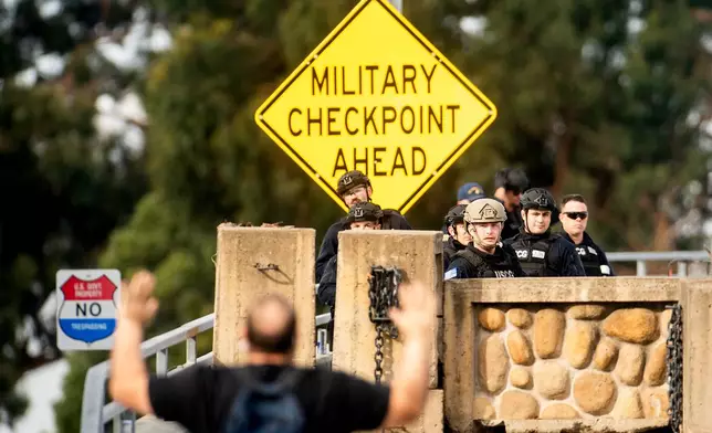Coast Guardsmen stand watch behind a barrier at Coast Guard Base Alameda as an anti-ICE protester approaches on Friday, Oct. 24, 2025, in Oakland, Calif. The barrier was erected earlier in the day after law enforcement officers fired on a vehicle as it backed towards them. (AP Photo/Noah Berger)