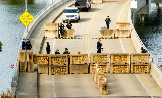Coast Guardsmen stand watch behind a barrier at Coast Guard Base Alameda on Friday, Oct. 24, 2025, in Oakland, Calif. The barrier was erected earlier in the day after law enforcement officers fired on a vehicle as it backed towards them. (AP Photo/Noah Berger)