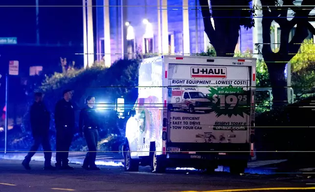 Police officers examine a U-Haul truck involved in a shooting at the entrance to Coast Guard Base Alameda, according to an officer at the scene, on Friday, Oct. 24, 2025, in Oakland, Calif. . (AP Photo/Noah Berger)