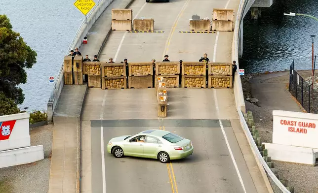 Coast Guardsmen stand watch behind a barrier at Coast Guard Base Alameda on Friday, Oct. 24, 2025, in Oakland, Calif. The barrier was erected earlier in the day after law enforcement officers fired on a vehicle as it backed towards them. (AP Photo/Noah Berger)