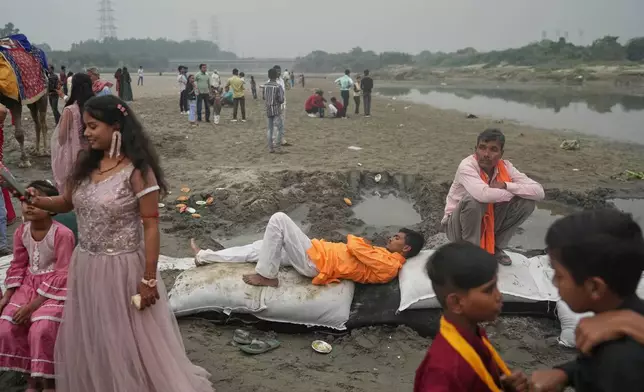 A person rests on the sand bags as devotees arrive on the banks of the river Yamuna during Chhath festival, which is celebrated for the well-being and prosperity of one's family, in New Delhi, India, Monday, Oct. 27, 2025. (AP Photo/Manish Swarup)