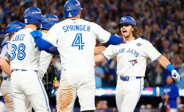 Toronto Blue Jays' Addison Barger, right, celebrates with teammates George Springer (4), Nathan Lukes, front left, and Andrés Giménez (obscured) after hitting a grand slam against the Los Angeles Dodgers during the sixth inning of Game 1 of baseball's World Series in Toronto, Friday, Oct. 24, 2025. (Frank Gunn/The Canadian Press via AP)
