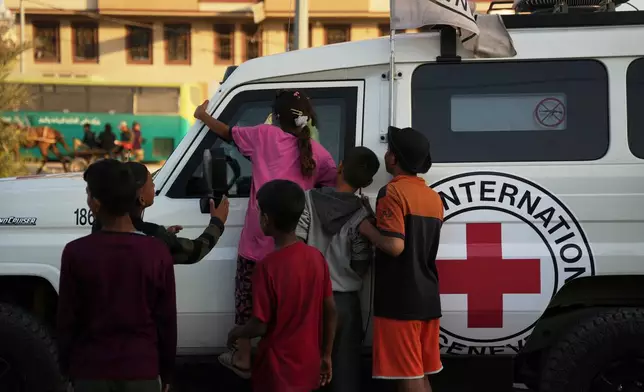 Palestinian kids look into a Red Cross vehicles carrying the bodies of two people believed to be deceased hostages handed over by Hamas make their way toward the Kissufim border crossing with Israel, to be transferred to Israeli authorities, in Deir al-Balah, central Gaza Strip, Thursday, Oct. 30, 2025. (AP Photo/Abdel Kareem Hana)