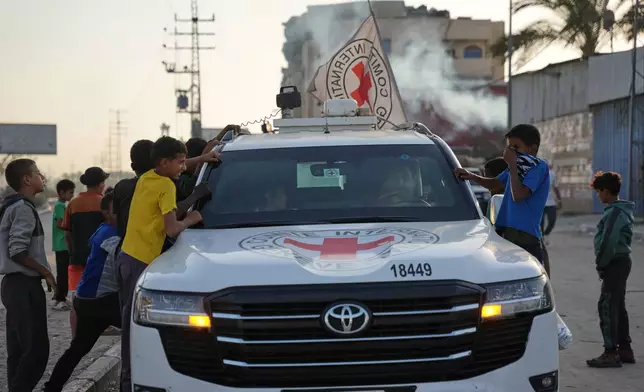 Palestinian kids look into a Red Cross vehicles carrying the bodies of two people believed to be deceased hostages handed over by Hamas make their way toward the Kissufim border crossing with Israel, to be transferred to Israeli authorities, in Deir al-Balah, central Gaza Strip, Thursday, Oct. 30, 2025. (AP Photo/Abdel Kareem Hana)