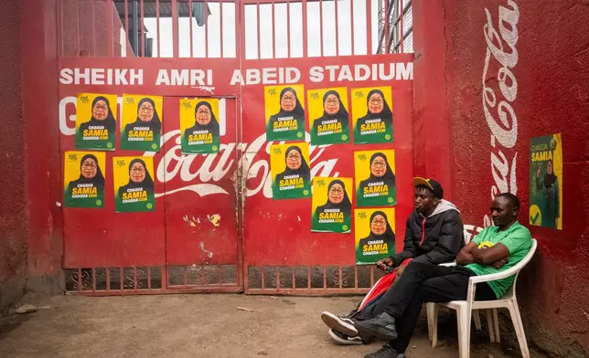 Men sit in front of campaign posters for Tanzanian presidential candidate Samia Suluhu Hassan, of the ruling Chama Cha Mapinduzi party, in Arusha, Tanzania, Oct. 8, 2025. (AP Photo)