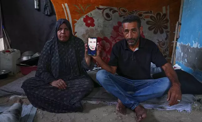 Mohammad and Tahani al-Najjar hold a cellphone showing a picture of their son, Ahmad, at their family's tent in Muwasi, along Gaza's southern coast, Feb. 22, 2025. Nearly two years after Ahmad went missing following Israeli bombardment, the al-Najjars are still searching for him. (AP Photo/Jehad Alshrafi)
