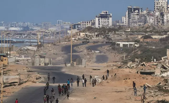 Israeli tanks block the beach road to Gaza City as displaced Palestinians gather on the coastal road near Wadi Gaza after the announcement that Israel and Hamas had agreed to the first phase of a peace plan to pause the fighting, in the central Gaza Strip, Thursday, Oct. 9, 2025. (AP Photo/Abdel Kareem Hana)