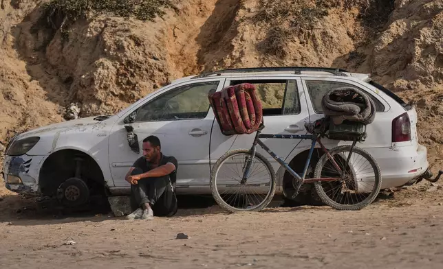 A displaced Palestinian man sits beside a bicycle as he waits on the coastal road near Wadi Gaza in the central Gaza Strip, Thursday, Oct. 9, 2025, during an attempt to return to Gaza City after the announcement that Israel and Hamas had agreed to the first phase of a peace plan to pause the fighting. (AP Photo/Abdel Kareem Hana)