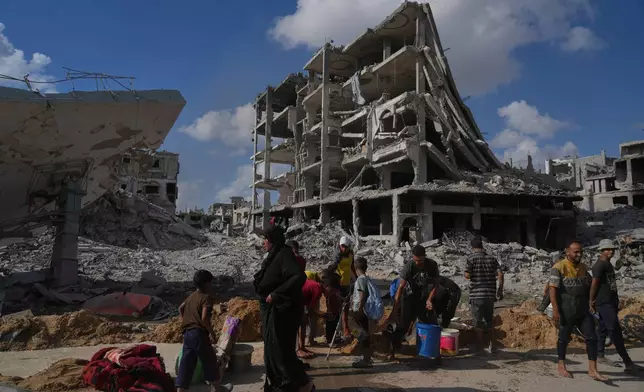 Palestinians collect water from a broken pipe surround destroyed buildings in Gaza City, Sunday, Oct. 12, 2025, after Israel and Hamas agreed to a pause in their war and the release of the remaining hostages. (AP Photo/Jehad Alshrafi)